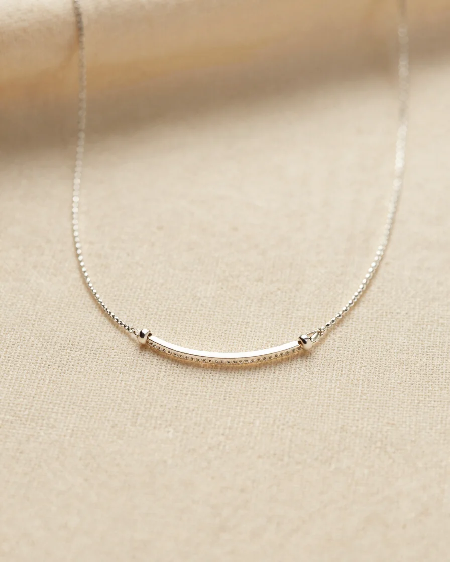 Macro close-up shot of a delicate silver necklace resting on textured warm cream linen, soft diffused daylight, warm min